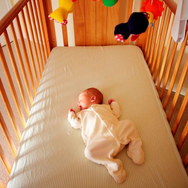 Ребенок лежит в детской кроватке на матрасе