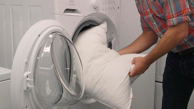 Мужчина кладет подушку в стиральную машину