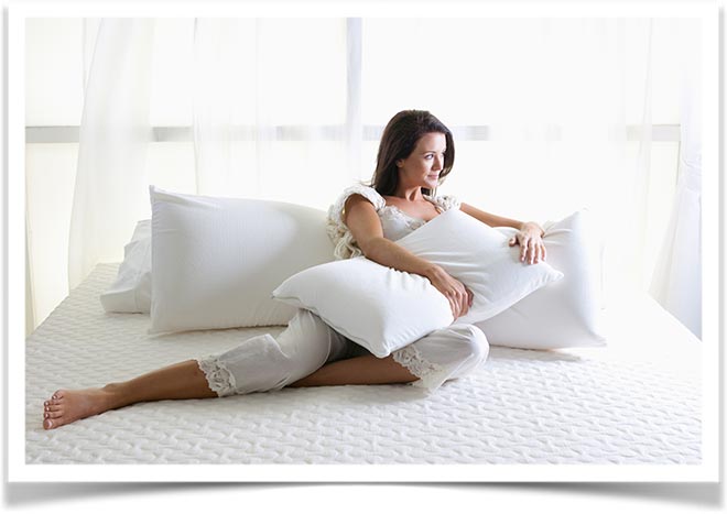 Женщина сидя на матрасе облокотилась на подушки