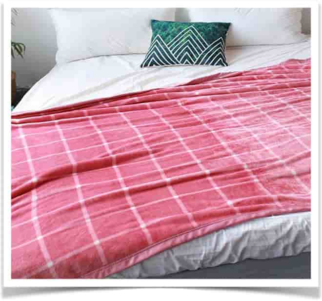 На белой кровати лежит красное одеяло в клетку и зеленя подушка